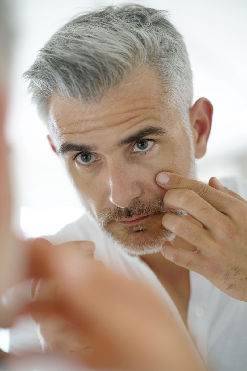 Middle-aged man applying cosmetic on his face, mirror view